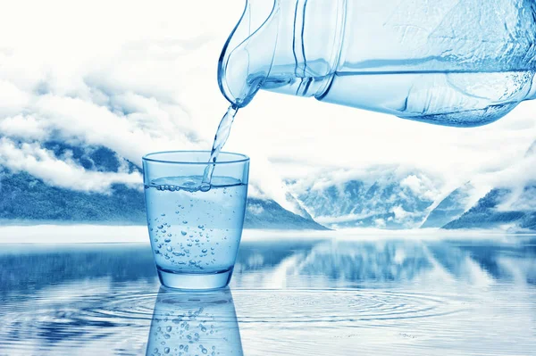 新鮮な冷たい水を瓶から自然景観に対するガラスに注ぐ — ストック写真