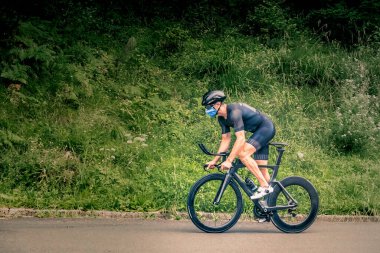 Triatlon 'a bisikletle katılan bir adam dağ bölgesinde Covid virüsüne karşı maskeli.