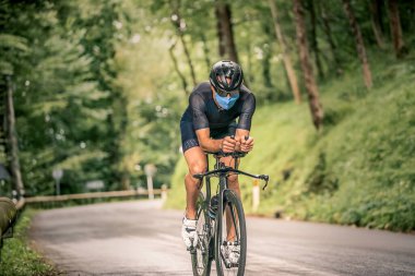 Triatlon 'a bisikletle katılan bir adam dağ bölgesinde Covid virüsüne karşı maskeli.