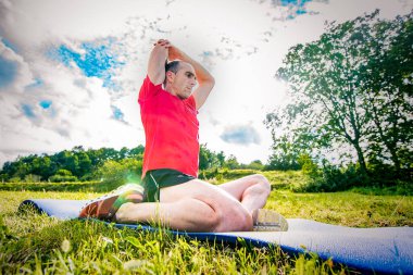 Atletik adam kırmızı gömlekli ve maskeli olarak doğada esneme hareketleri yapıyor.