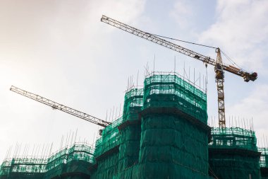 İnşaat vinçleri ve inşaat halindeki bina güneşli gökyüzüne karşı