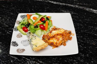 Akşam yemeği tabağı lazanya ve salata, granit masada..
