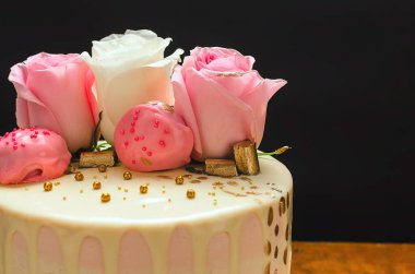 Doğal güller ve çikolatalarla süslenmiş güzel bir pasta, ahşap masanın üzerinde. Ev yapımı..