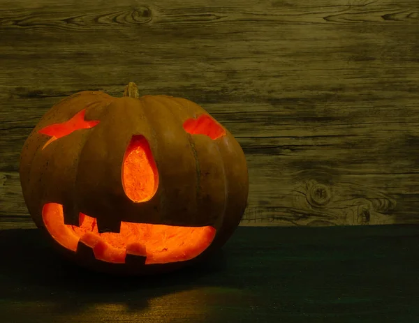 Lighted pumpkin lantern on green table and wooden background.