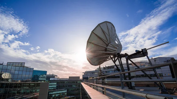 Satellite dish on a modern office building, blue sky and setting sun. Concept of long distance communication.