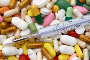 Termometre 37 C dereceye işaret ediyor. Tabletler, kapsüller ve farklı renk ve renkte haplar. Yakın plan. İlaç, hastalık, ateş ve tedavi kavramı