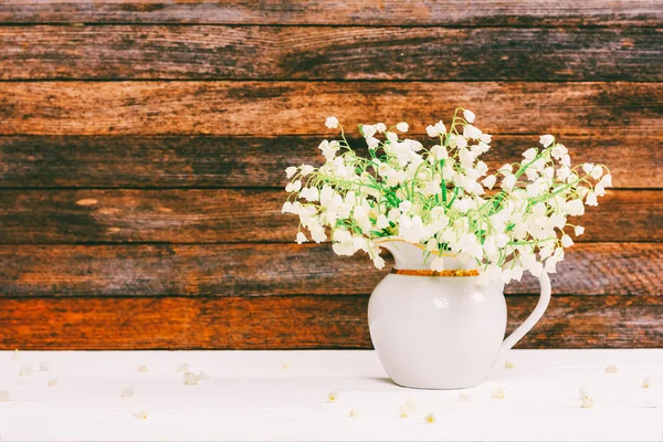 bouquet of Lily of the valley flowers in a jug on a white wooden table on a retro grunge wall background with copy space