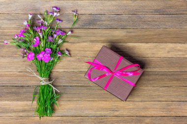 bouquet of carnations and brown box with a gift on a wooden background, flat lay top view clipart