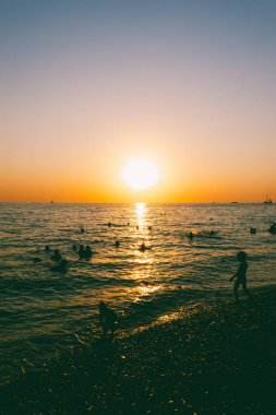 insanlar akşam günbatımında denizde yüzmek