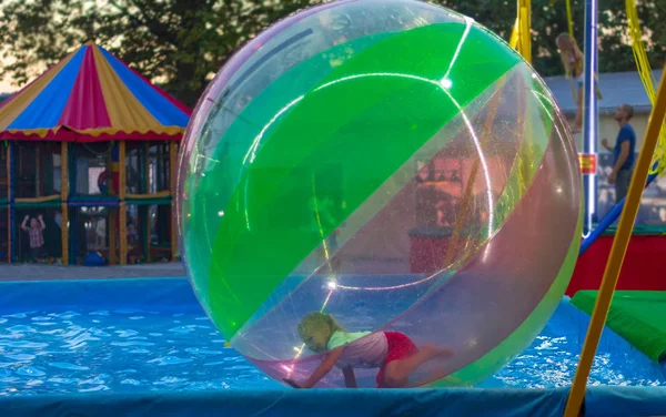 Niña de 5-8 años jugando en un globo grande en el agua en la piscina en el parque de atracciones —  Fotos de Stock