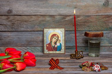 Maikop, Rusya - 13 Nisan 2018: 9 Mayıs 1945 zafer günü kutlaması, madalyalar, Ortodoks simgesi ve yanan kırmızı mum, kırmızı lale çiçek buketi ve çavdar ekmeği ile bir bardak votka