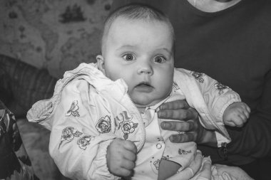 annesinin kollarında oturan dört aylık bir kız bebek portresi, siyah beyaz fotoğraf