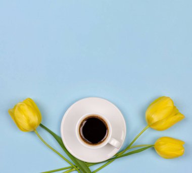 bir tabak üzerinde siyah kahve bir Fincan ve kopya alanı ile mavi bir arka plan üzerinde sarı bir Lale çiçek, yakın çekim üst görünüm düz yatıyordu