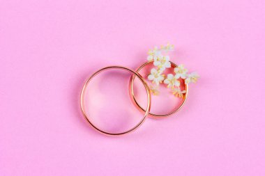 altın alyans lar ve pembe bir arka plan üzerinde bir yüzük küçük beyaz çiçekler bir çift, üst görünüm düz yatıyordu