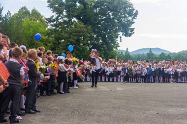 Adygea, Rusya - 1 Eylül 2018: okul yılının büyük açılışında kollarında birinci sınıf öğrencisi olan lise öğrencisi ve okul bahçesindeki diğer okul çocukları