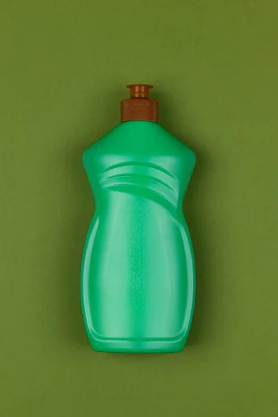light green plastic bottle of dishwashing liquid on dark green background close-up top view