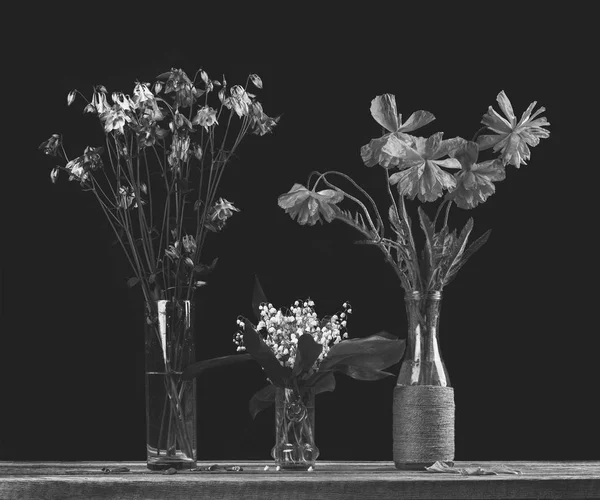 bouquet of flowers of poppies, a bouquet of white lilies of the valley and a bouquet of flowers of bluebells in glass vases on a black background, black and white photo