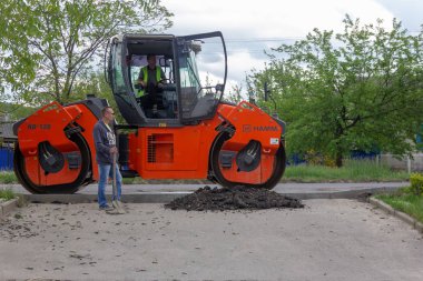 Kamennomostsky, Rusya - 10 Mayıs 2019: Elinde kürek olan bir adam asfalt kompaktör silindiri Hamm hakkında