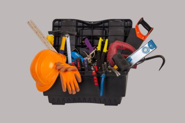 Gri arka planda izole edilmiş, turuncu bir miğferi ve çeşitli el aletleri olan açık siyah plastik bir alet çantası.