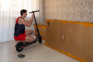 Genç bir adam dairede elektrikli scooter monte ediyor.