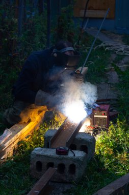 Erkek kaynakçı akşamları yazlık evlerinde elektrik kaynaklarıyla çelik parçaları kaynaklıyor.