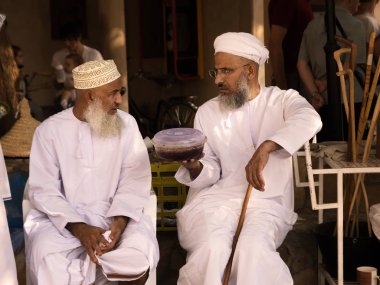 Nizwa, Umman - 2 Kasım 2018: Omani adam başka bir adamla Nizwa piyasada geleneksel giysiler içinde Halwa paketi eller