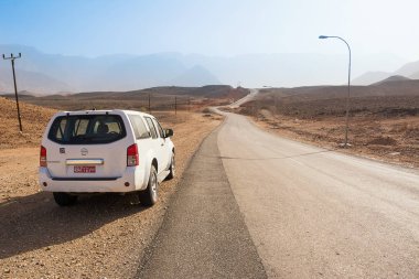 Qurayyat, Umman - 4 Kasım 2018: Asfalt yol Omani kayalık çöl ve güneşli bir günde 4 x 4 araba