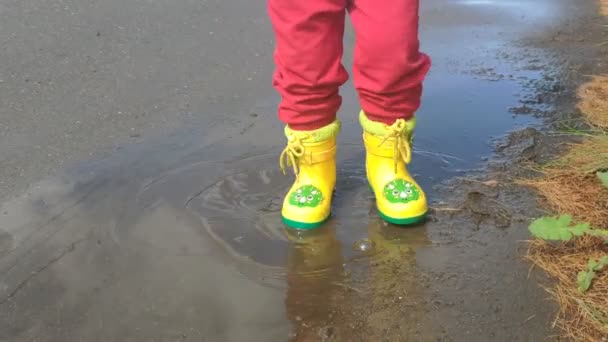 A criança está rindo e pisando através de poças em botas amarelas — Vídeo de Stock