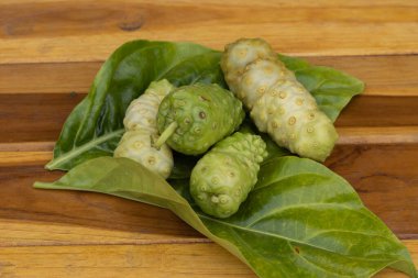 Otlar, yenilebilir yaprakların üzerinde taze noni güzel ahşap bir arka plana yerleştirilir..