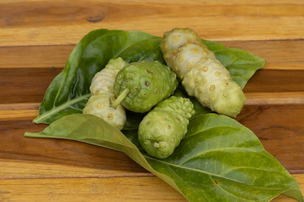 Otlar, yenilebilir yaprakların üzerinde taze noni güzel ahşap bir arka plana yerleştirilir..