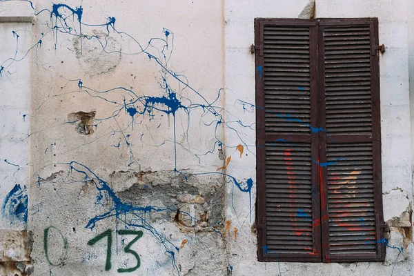 Persianas marrones de madera cerradas en pared de textura gruesa. Salpicaduras de pintura azul y roja en la pared. Persianas de madera cerradas antiguas — Foto de Stock