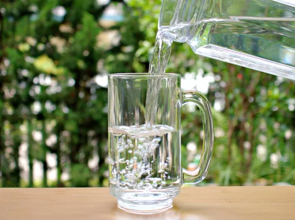 Bulanık arka planda içme suyu bir sürahide bardağa dökülür., 