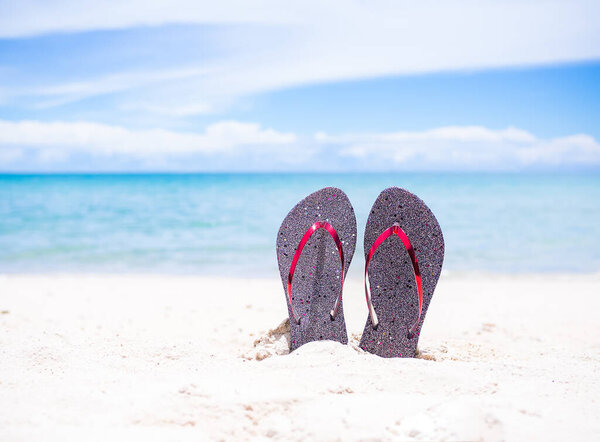 Шлепанцы на песчаном пляже с размытым изображением синего моря и голубого неба. для содержит статьи о море или путешествовать летом в отпуске.