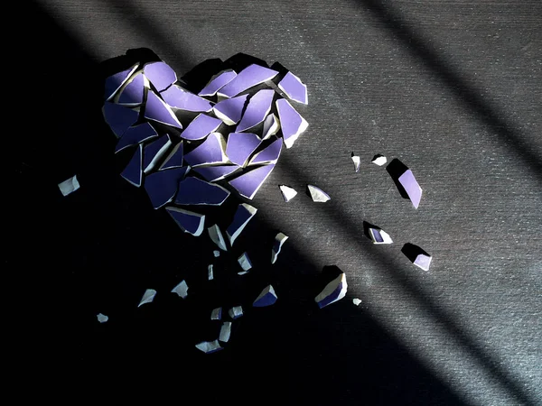 Broken heart concept. Purple broken glass on dark black background with light shadow.