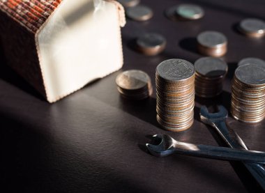 Ev konseptini değiştirmek için 2021 yılı tasarruf etmeyi planlayın. Bozuk para, ingiliz anahtarı ve karanlık ahşap üzerine aydınlık arka planlı model evi..