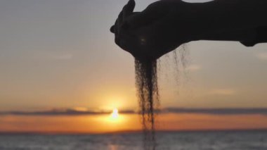 Kum, Deniz Günbatımına Karşı Eller 'in siluetinde akıyor. Dünyada Yaşam Boyu Geçici Kavramı