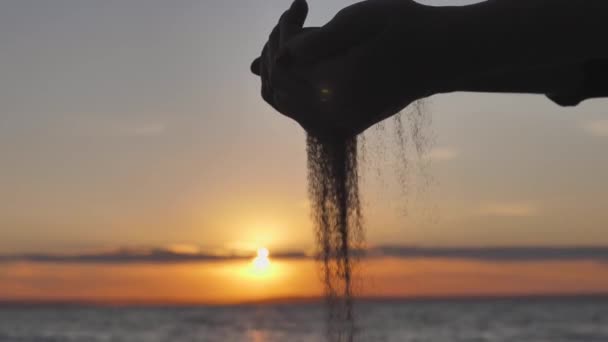 Piasek przepływający przez sylwetkę rąk przed zachodem słońca. Koncepcja przemijającego życia na Ziemi — Wideo stockowe