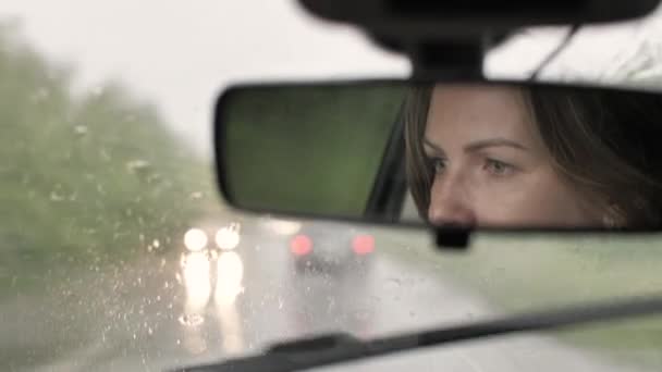 Mladý kavkazský žena řízení auto ve zpětném zrcátku v silném dešti — Stock video