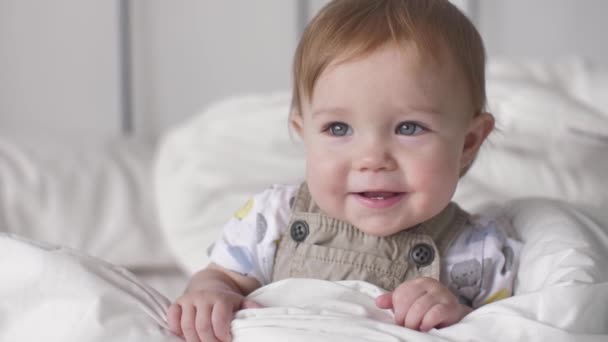 Прекрасний маленький кавказький хлопчик посміхається портрет немовляти сміється на ліжку вдома — стокове відео