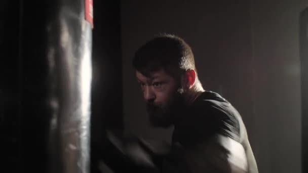 Жорстокий боксер сильний спортсмен хіти мішок на темному тлі в тренажерному залі — стокове відео