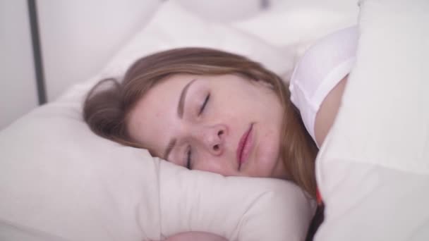 Mujer joven que duerme bien en una cómoda y acogedora cama sobre ropa de cama de almohada blanca, sueño profundo saludable — Vídeo de stock