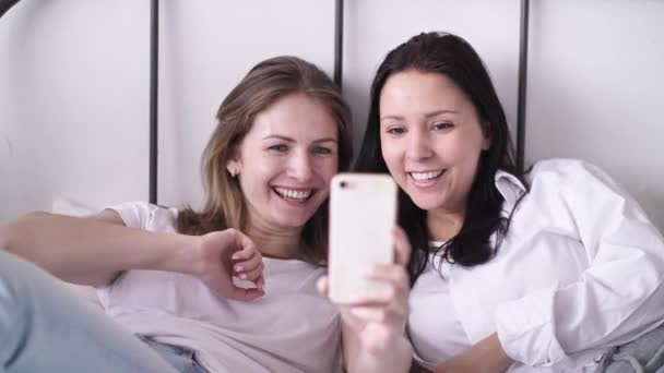 Две молодые женщины, делающие селфи-портрет на телефоне, показывают положительные эмоции на лице, смеются, размахивая руками, веселясь. — стоковое видео