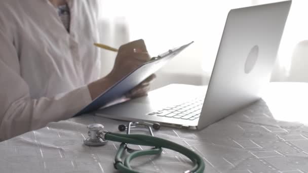 病院の医療室でノートパソコンやライティングを担当する医師。聴診器に焦点を当てる — ストック動画