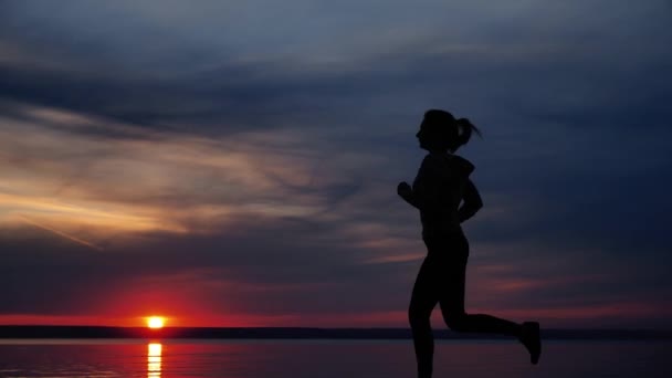 Γυναίκα τρέχει μόνη στο όμορφο ηλιοβασίλεμα στην παραλία. Σιλουέτα εκπαίδευσης αθλητών στο Dusk — Αρχείο Βίντεο