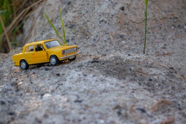 Sarı küçük araba modeli, kumdan geçerek nehir kıyısına gidiyor.