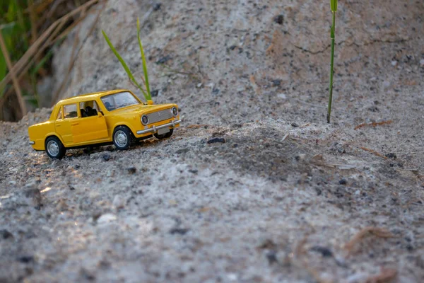 Sarı küçük araba modeli, kumdan geçerek nehir kıyısına gidiyor.