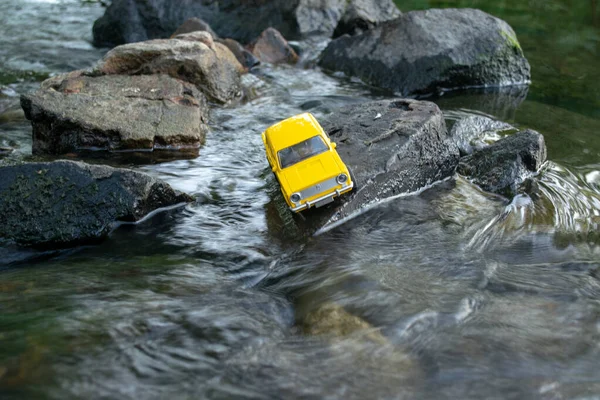 Sarı küçük araba taşların üzerinde karanlık nehirde ilerliyor.