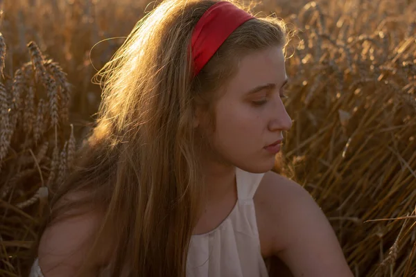 Güzel, uzun saçlı, buğday tarlasında oturan genç bir bayanın sıcak güneş ışınları.