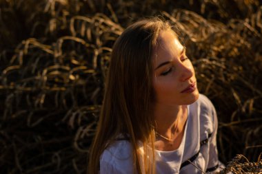 Genç bayan akşam güneşinin altında tarlada oturuyor.