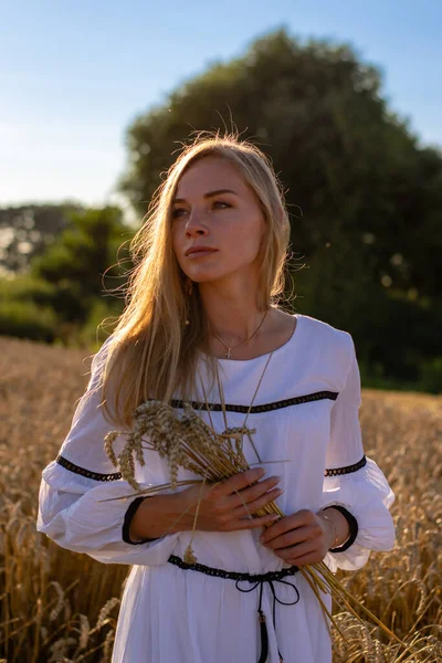 Beyaz uzun elbiseli genç bayan, elinde buğdayla tarlada.